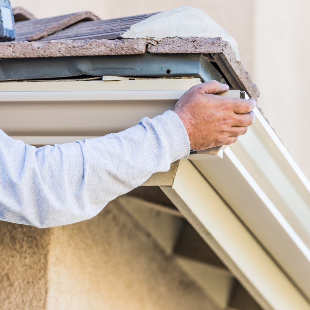 Worker Attaching Aluminum Rain Gutter to Fascia of House.